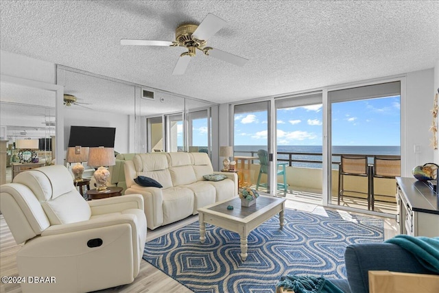 living room with expansive windows, a textured ceiling, ceiling fan, and light hardwood / wood-style flooring