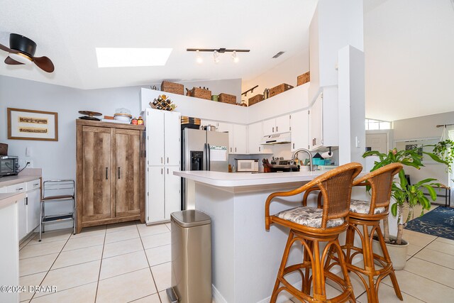 kitchen with stainless steel appliances, white cabinetry, a breakfast bar, kitchen peninsula, and lofted ceiling with skylight