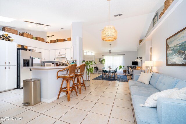 kitchen featuring lofted ceiling, kitchen peninsula, hanging light fixtures, light tile patterned floors, and white cabinetry