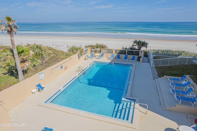 view of swimming pool featuring a water view, a beach view, and a patio