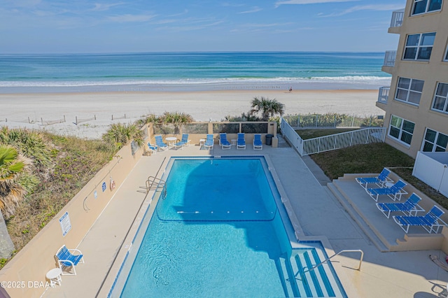 view of pool with a patio, a water view, and a view of the beach