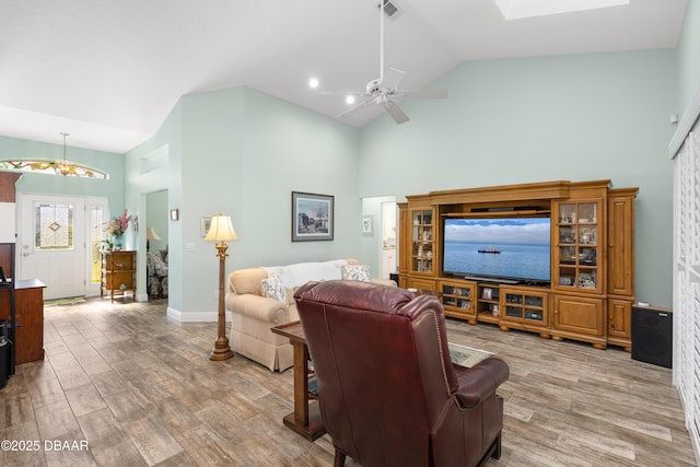 living room featuring hardwood / wood-style flooring, ceiling fan, a skylight, and high vaulted ceiling