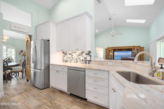 kitchen featuring sink, a skylight, stainless steel appliances, light stone counters, and white cabinets