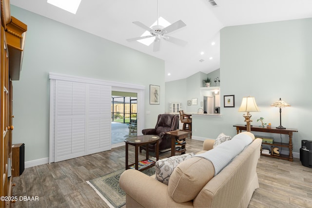 living room with a skylight, high vaulted ceiling, and light wood-type flooring