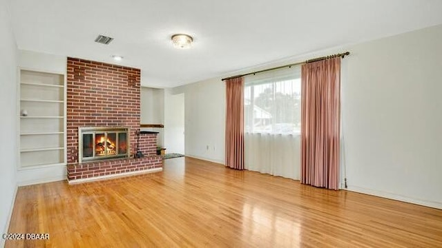 unfurnished living room featuring a brick fireplace, wood-type flooring, and built in shelves