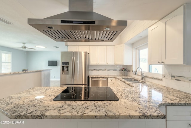 kitchen with island exhaust hood, light stone counters, stainless steel appliances, sink, and white cabinets