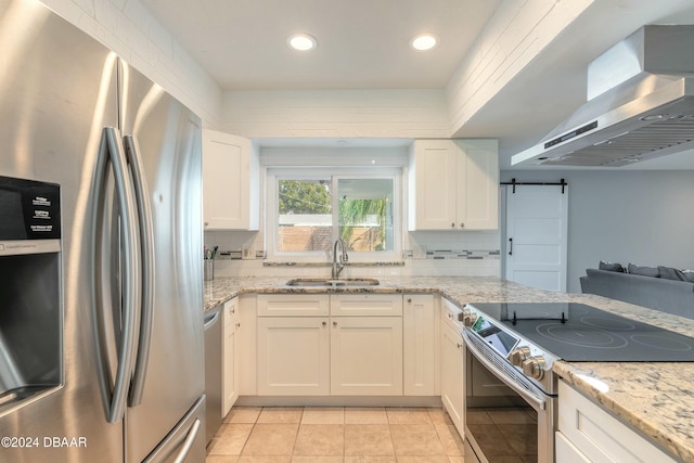 kitchen featuring wall chimney exhaust hood, stainless steel appliances, sink, a barn door, and white cabinets