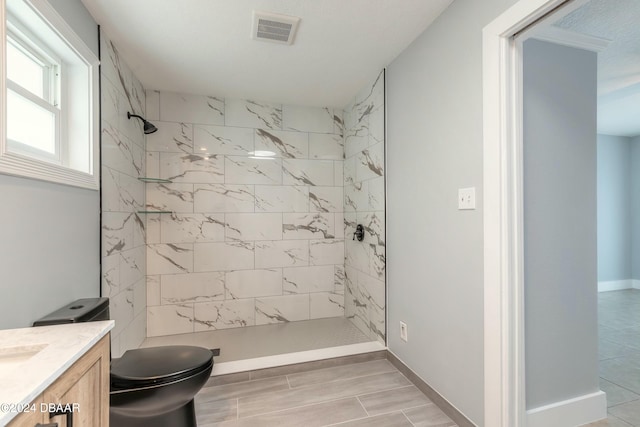 bathroom featuring a tile shower, vanity, and toilet