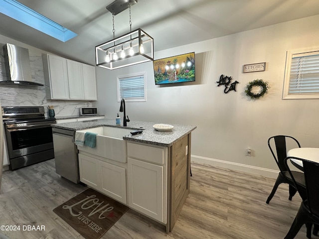 kitchen featuring white cabinetry, light stone countertops, wall chimney exhaust hood, a center island with sink, and appliances with stainless steel finishes