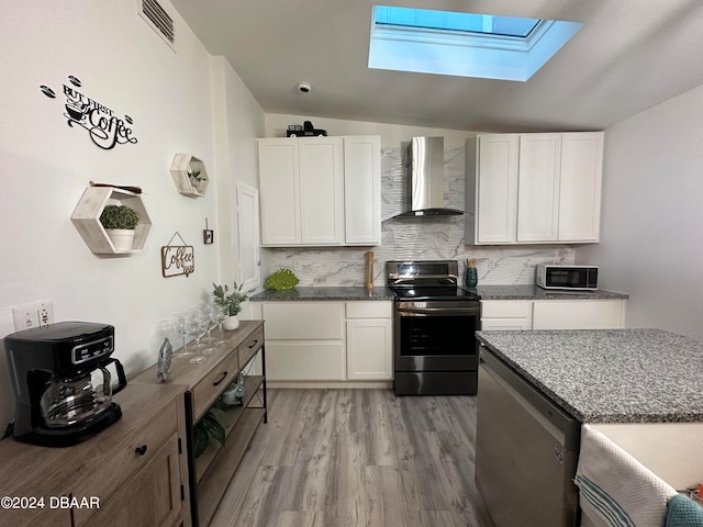 kitchen with white cabinetry, wall chimney range hood, appliances with stainless steel finishes, and lofted ceiling with skylight