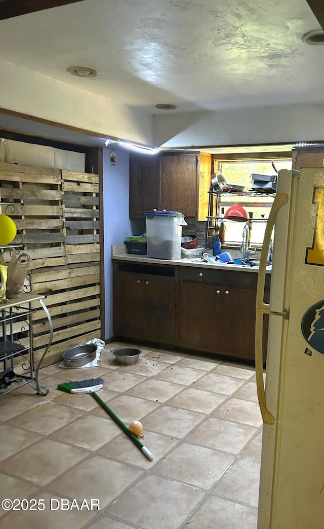kitchen featuring light countertops, freestanding refrigerator, and dark brown cabinetry