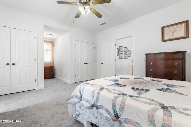 carpeted bedroom featuring ceiling fan, a textured ceiling, and two closets