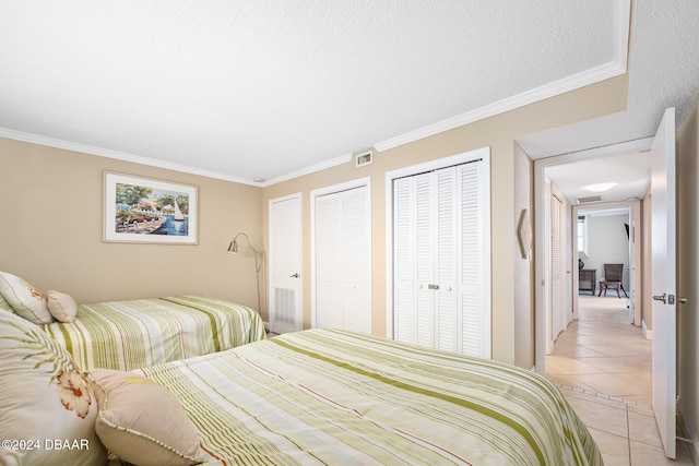 bedroom with a textured ceiling, light tile patterned floors, two closets, and crown molding