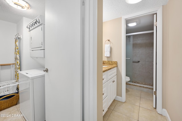 clothes washing area with stacked washing maching and dryer, a textured ceiling, and light tile patterned floors