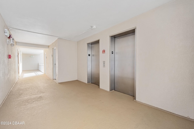 corridor featuring elevator and light colored carpet