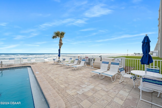 view of swimming pool with a patio, a water view, and a beach view