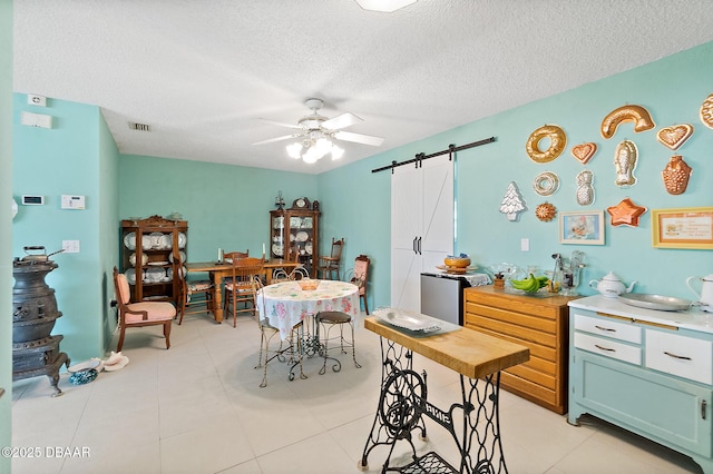 tiled dining space featuring ceiling fan, a barn door, and a textured ceiling