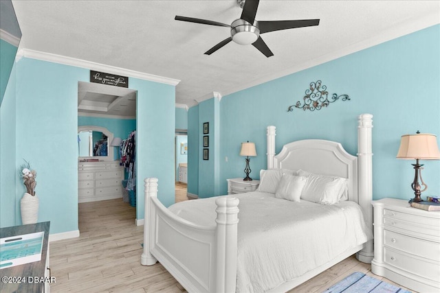 bedroom featuring crown molding, a walk in closet, light hardwood / wood-style flooring, a textured ceiling, and ceiling fan