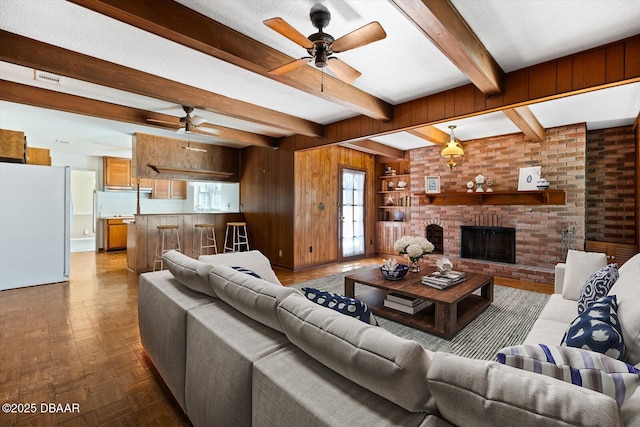 living room with a fireplace, wooden walls, parquet floors, a textured ceiling, and beam ceiling