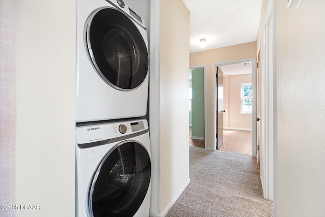 clothes washing area featuring stacked washer / drying machine and light carpet