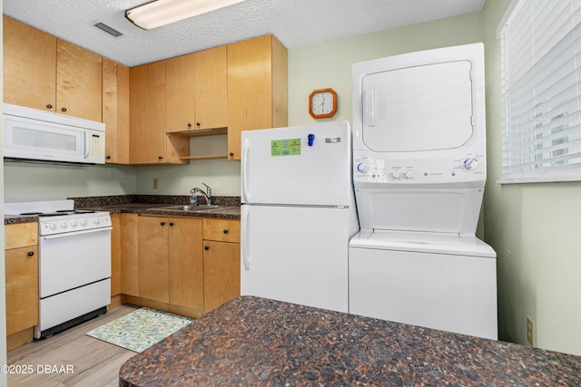 kitchen featuring sink, white appliances, stacked washer and clothes dryer, and a textured ceiling