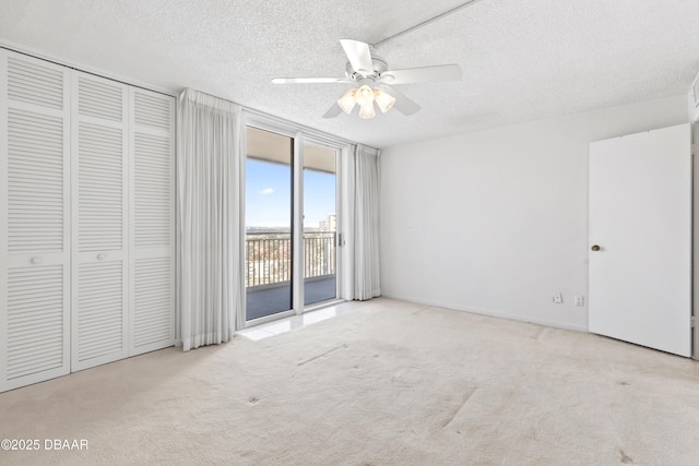 unfurnished bedroom featuring ceiling fan, light colored carpet, access to exterior, floor to ceiling windows, and a textured ceiling