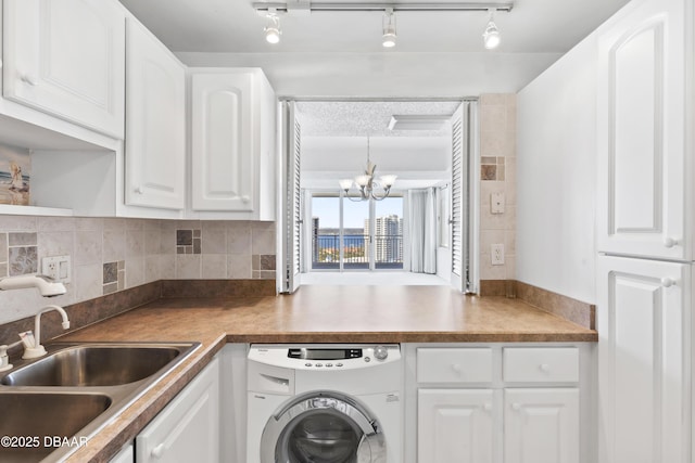 kitchen with washer / dryer, sink, an inviting chandelier, white cabinetry, and track lighting