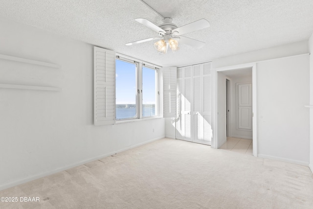 carpeted empty room featuring ceiling fan, a water view, and a textured ceiling