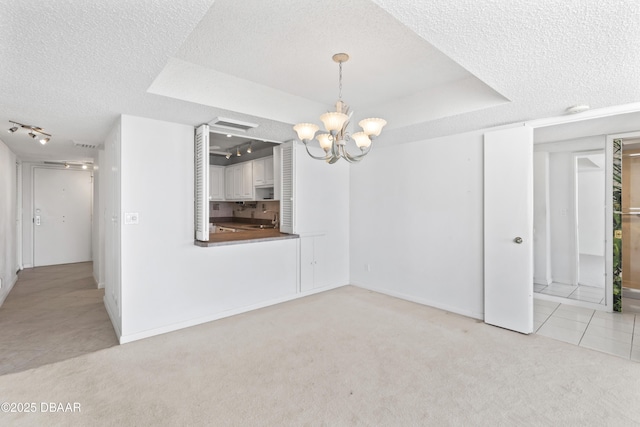 unfurnished dining area featuring light colored carpet, a notable chandelier, sink, and a tray ceiling