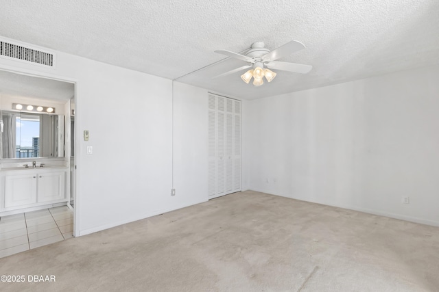 unfurnished room with a textured ceiling, ceiling fan, light colored carpet, and sink