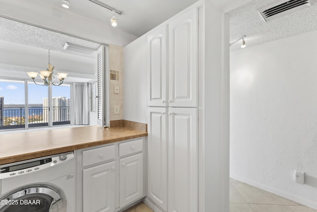 clothes washing area featuring a notable chandelier, washer / dryer, a textured ceiling, light tile patterned floors, and cabinets