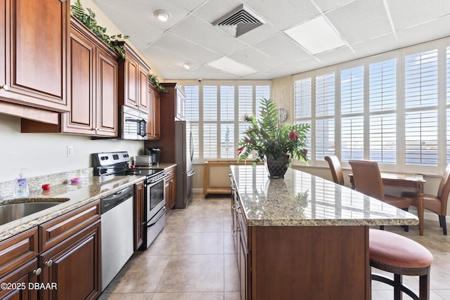 kitchen with a drop ceiling, appliances with stainless steel finishes, plenty of natural light, and a center island