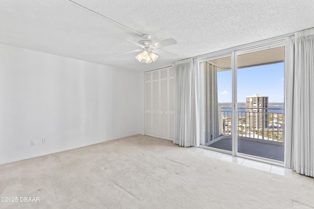 empty room featuring ceiling fan, expansive windows, light carpet, and a textured ceiling