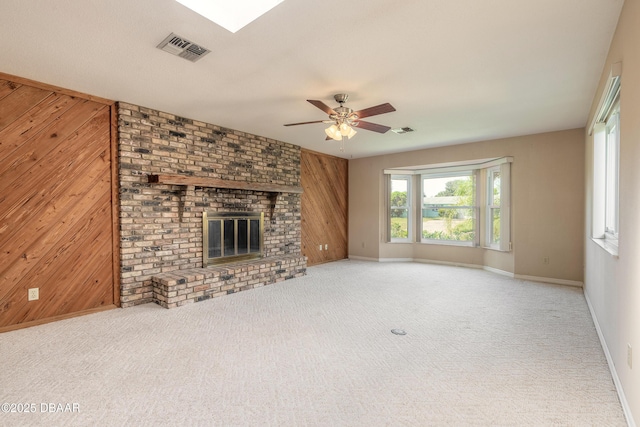 unfurnished living room with ceiling fan, wooden walls, a fireplace, and carpet flooring