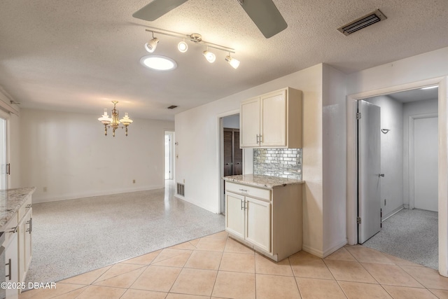 kitchen featuring light stone counters, backsplash, ceiling fan with notable chandelier, and a textured ceiling