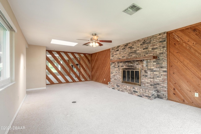 unfurnished living room featuring a fireplace, plenty of natural light, wooden walls, and light colored carpet