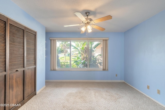 unfurnished bedroom featuring ceiling fan, light colored carpet, a textured ceiling, and a closet