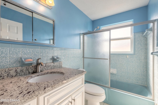 full bathroom with tile walls, shower / bath combination with glass door, vanity, toilet, and a textured ceiling