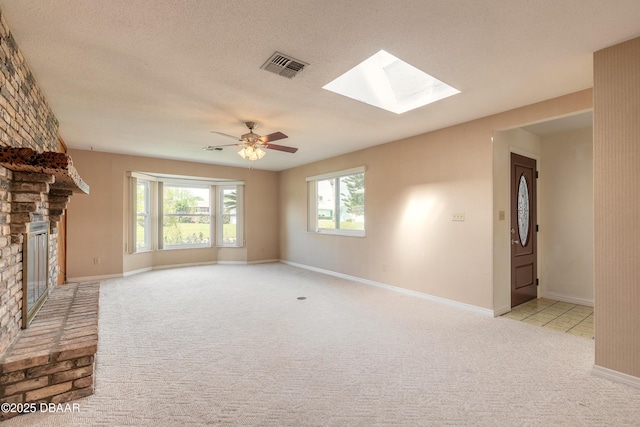 unfurnished living room featuring light colored carpet, a textured ceiling, a fireplace, and a skylight