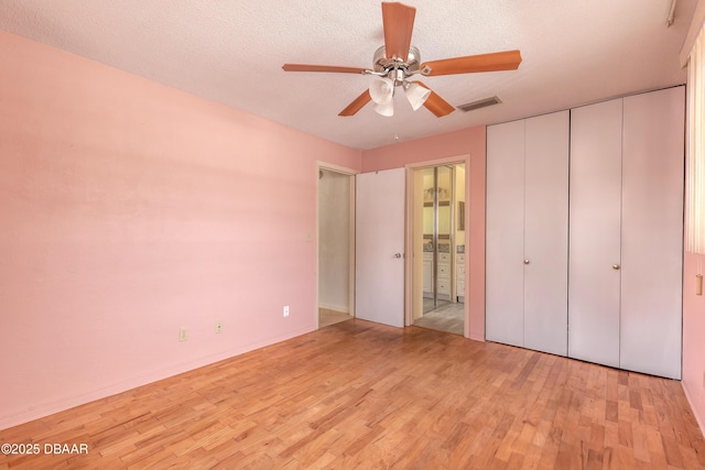 unfurnished bedroom featuring ceiling fan, a textured ceiling, light hardwood / wood-style floors, and ensuite bath