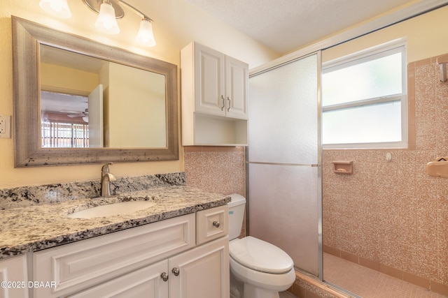 bathroom with a shower with door, vanity, ceiling fan, and toilet