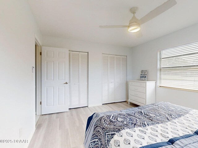 bedroom featuring light wood-type flooring, baseboards, a ceiling fan, and multiple closets