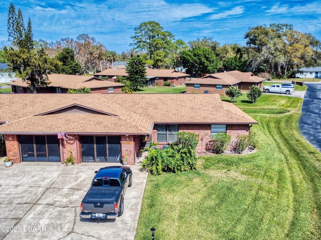 single story home with a shingled roof, a front yard, concrete driveway, and brick siding