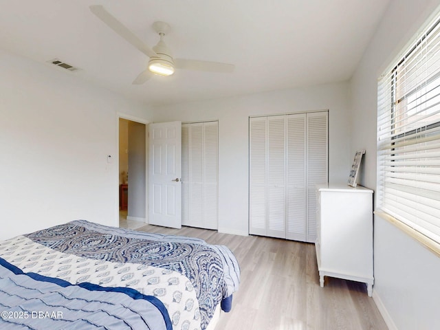 bedroom with baseboards, visible vents, ceiling fan, light wood-style floors, and multiple closets