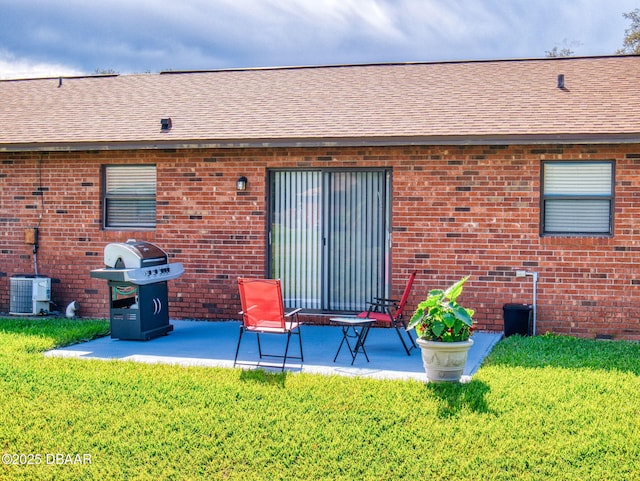 back of house featuring roof with shingles, a patio, a lawn, and brick siding