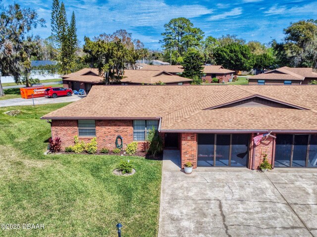 single story home featuring driveway, brick siding, a shingled roof, and a front yard