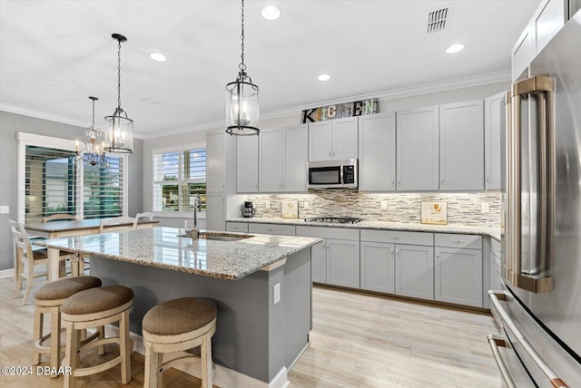 kitchen featuring stainless steel appliances, sink, light stone countertops, decorative light fixtures, and an island with sink