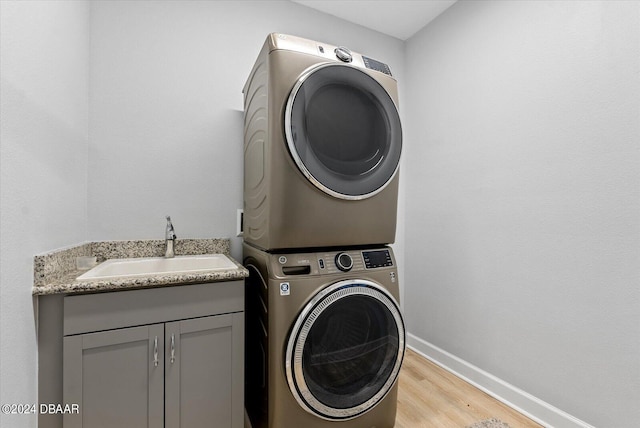 laundry area featuring stacked washing maching and dryer, light hardwood / wood-style floors, cabinets, and sink