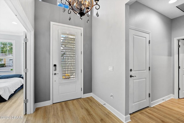 foyer entrance with ornamental molding, light wood-type flooring, and a notable chandelier