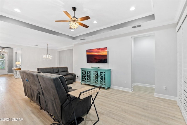 living room featuring ornamental molding, ceiling fan with notable chandelier, light hardwood / wood-style flooring, and a tray ceiling